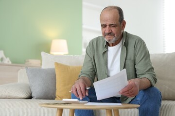 Fototapeta premium Pension. Senior man with money, calculator and paperwork at table indoors. Space for text
