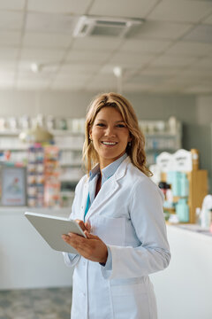 Happy female pharmacist with digital tablet in drugstore looking at camera.