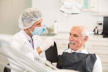 Fototapeta premium Adult male dentist showing elderly male patient result of dental procedure in dental clinic