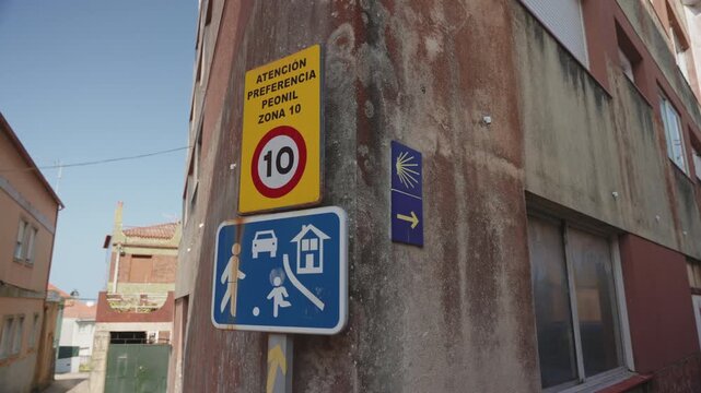 Street scene in a Spanish town showing traffic signs, including a pedestrian zone indicator and a Camino de Santiago waymarker.