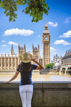 Rear view of a tourist woman standing in front of the Big Ben clock tower in London, England, during a sunny summer day