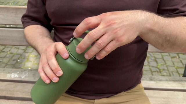 Close up of hands closing reusable water bottle outdoors after refill. Eco lifestyle, hydration and sustainable zero waste living concept.