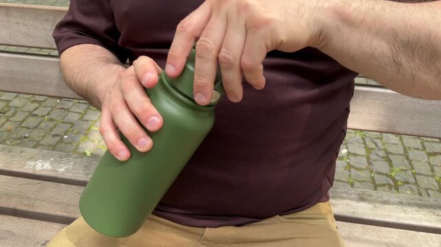 Close up of hands unscrewing reusable water bottle outdoors. Eco lifestyle, hydration, sustainability and zero waste daily routine concept.