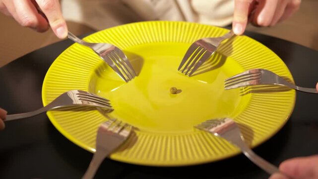 People fighting for a single pea on a plate with forks. Multiple hands with forks fighting over one single green pea on a yellow plate, a conceptual video about competition, scarcity of resource