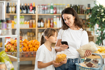 Mother and daughter checks expiration date of cornflakes and oat flakes - scans QR code on label...