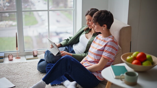 Two friends shopping online using tablet sitting floor living room. Couple women