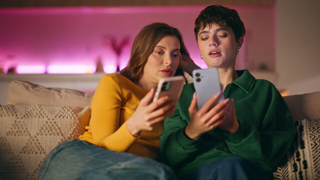 Friends discussing social media news looking cellphones sitting couch closeup.