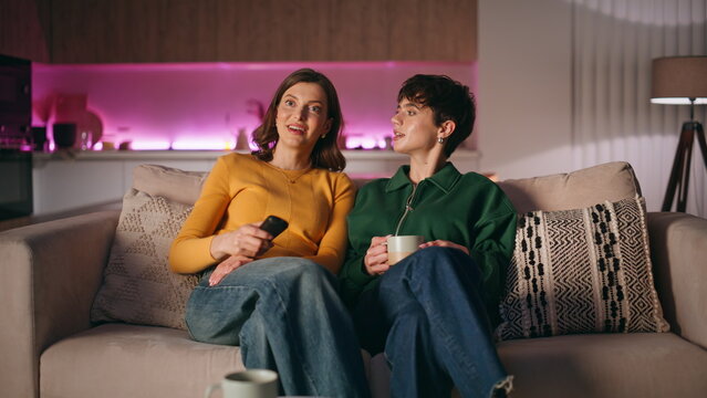Relaxed women watching television sitting cozy apartment couch. Carefree ladies