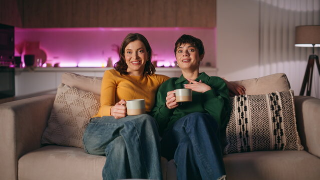 Two ladies enjoy comedy show sitting home couch. Happy women watching television