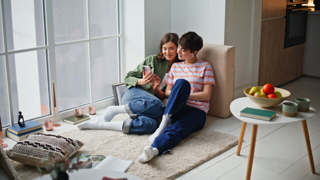 Friends watching phone content together spending weekend home. Smiling besties