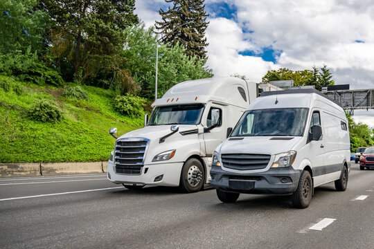 Big rig white semi truck with semi trailer and cargo commercial mini van running on the highway road side by side
