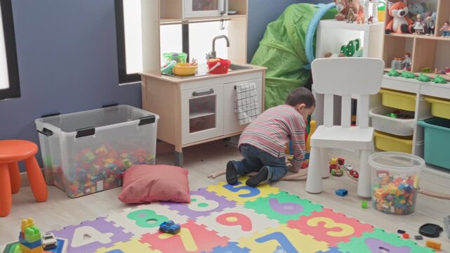 Boy kneeling playing with a toy car on a colorful number foam mat inside a building playroom; playful curiosity.