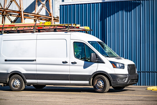 Cargo minivan with ladders on the roof standing on the industrial business side parking lot