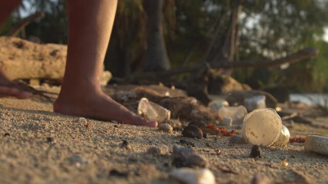 Bare Feet Walking Along a Sandy Beach Scattered with Plastic Cups and Marine Debris, Highlighting Coastal Pollution, Environmental Damage, Ocean Conservation, and the Urgent Need for Sustainable Waste