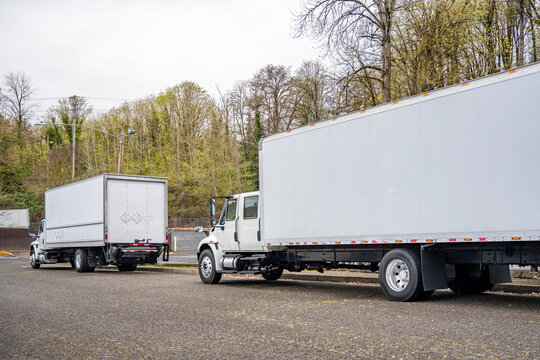 Day cab middle duty white semi trucks with roomy bo trailer standing on the street waiting for the next commercial cargo