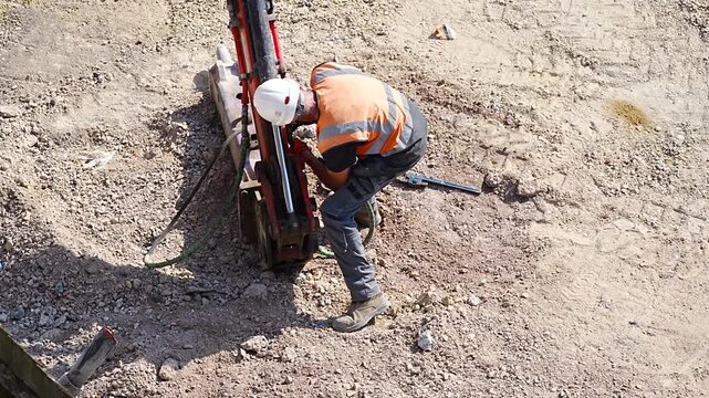 Worker in orange vest operating drill machine at outdoor excavation work site