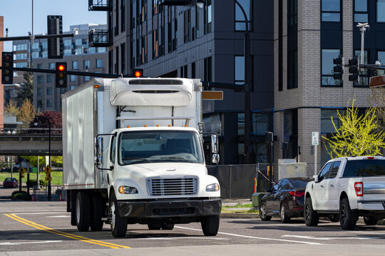 Middle duty day cab rig semi truck with refrigerator bo trailer transporting cargo running on the urban city crossroad with traffic lights