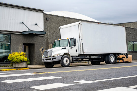 Popular day cab middle duty rig semi truck with long box trailer unloading cargo standing on the city street