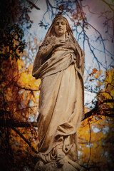Obraz premium Graceful angel statue standing among autumn trees, symbolizing hope, faith and divine protection.