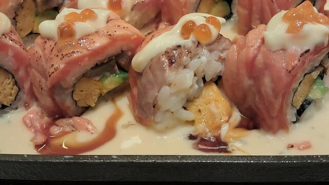 A horizontal close up video tracking along a row of bacon wrapped rolls cooking on a restaurant grill.
