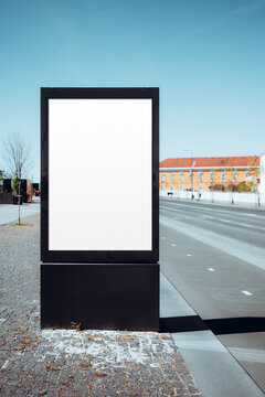 Tall blank advertising lightbox mockup beside a quiet city road and bike lane, with clear poster space for outdoor media, cycling route branding or urban campaign display