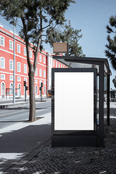 Empty backlit poster panel on black bus stop shelter beside red historic building and trees, ideal for urban advertising mockup, campaign preview or branding template