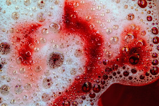 Schiuma da detergente con bolle e bollicine colorate in liquido rosso