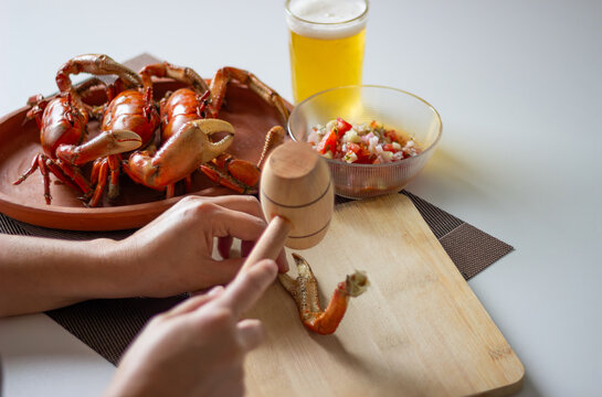 Person cracking crab claw with wooden mallet and beer