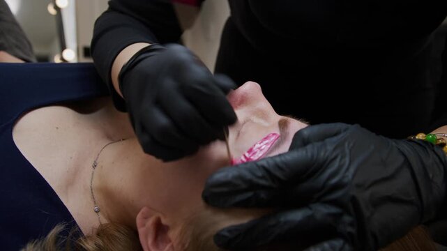 Watch as a skilled beautician expertly applies permanent makeup to enhance brows using a tattoo machine. This close-up reveals the precision and care involved in the process