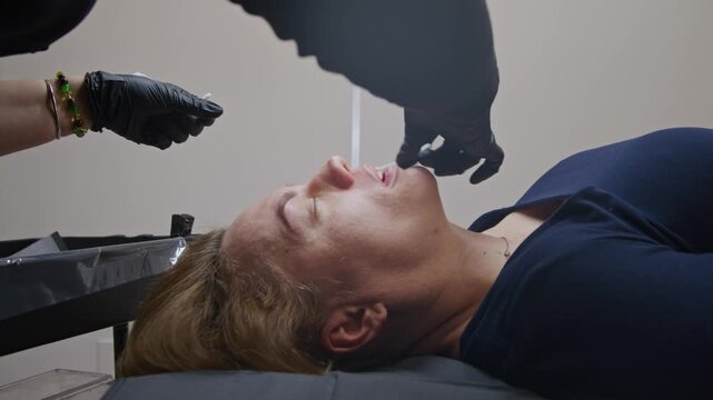 Close-up of a skilled beautician applying eyebrow tattoo using a needle machine. Witness the art of permanent makeup as colors blend beautifully for a flawless look at a salon