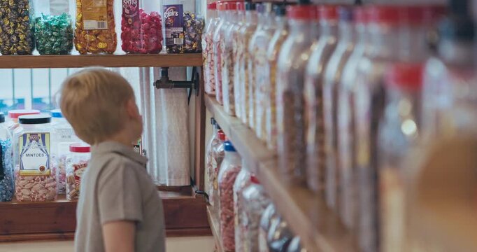 Kid, shopping in a candy store and choice of sweets, confectionery or boy in a retail supermarket, shop and sale of candies. Jar, shelf and child choosing product, chocolate or toddler with decision
