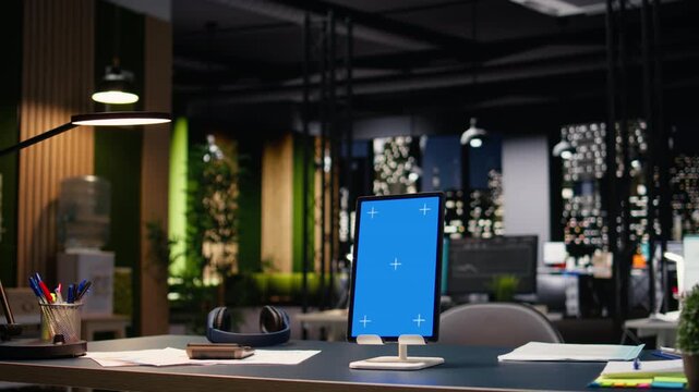 Vertical blue screen tablet in empty corporate office with spacious open space layout and elegant interior design. Professional workplace atmosphere in business headquarters after hours.