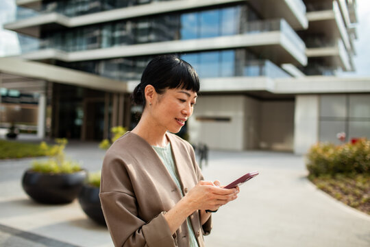 Smiling woman using smartphone outside modern office building