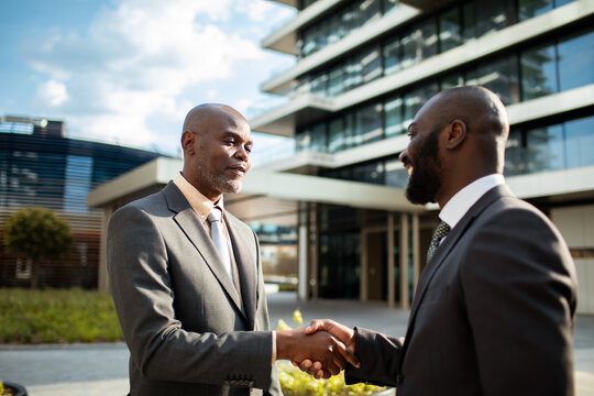 Two businessmen shaking hands outside modern office building
