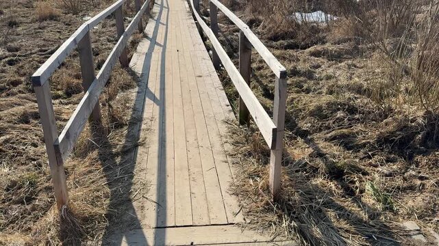 Temporary wooden bridge over dry grass, narrow plank walkway with handrails casting long shadows across dead brown vegetation
