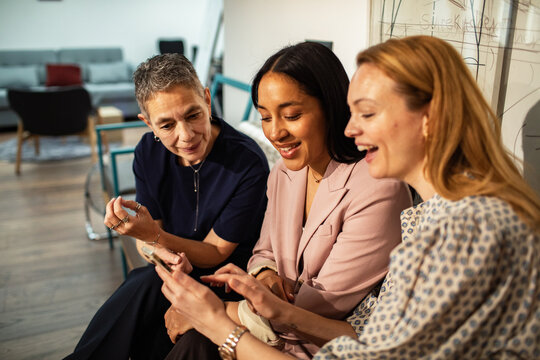 Three businesswomen collaborating on smartphone in modern office