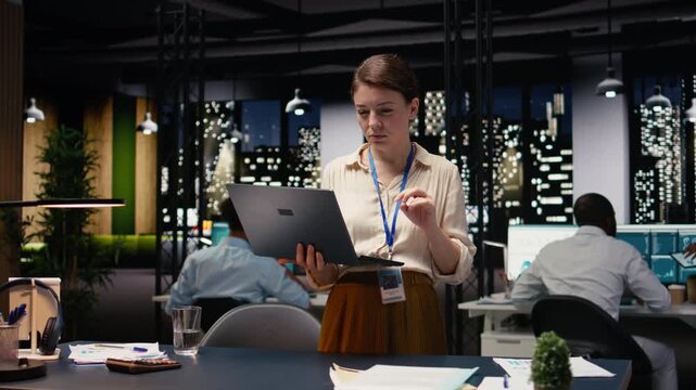 Portrait of smiling businesswoman coordinating daily administrative operations with laptop. Happy woman standing in office uses device to implement sales strategies increasing profitability.