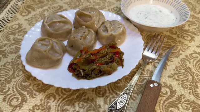 Manti dumplings on white plate homemade steamed dough parcels served with spicy vegetable salad and sesame garnish fork and knife