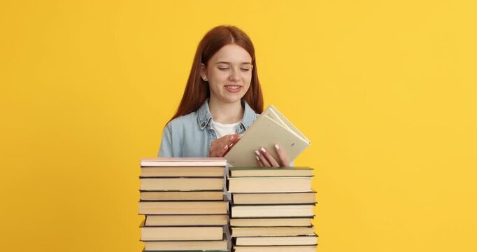 Teenage girl taking book from stack on yellow background