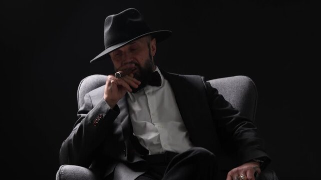 Mafia. Man smoking cigar in armchair against dark background
