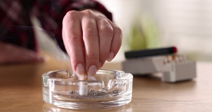 Woman flicking ash and putting out cigarette in ashtray at wooden table, closeup
