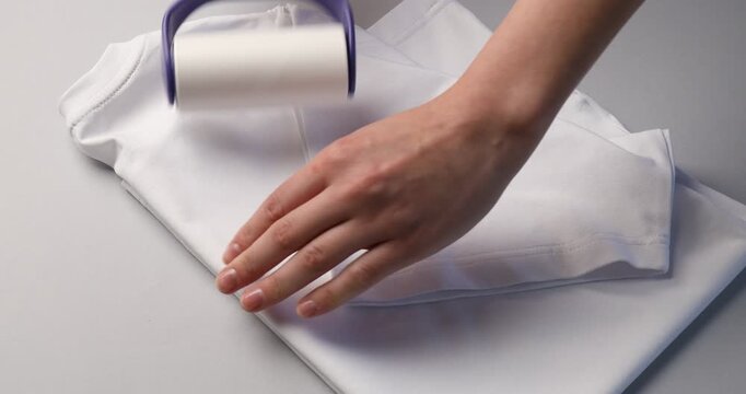 Woman cleaning t-shirt with lint roller on white background, closeup