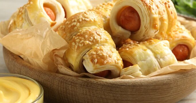 Puff pastry. Tasty sausages in dough and sauce on white wooden table, closeup. Camera moving right