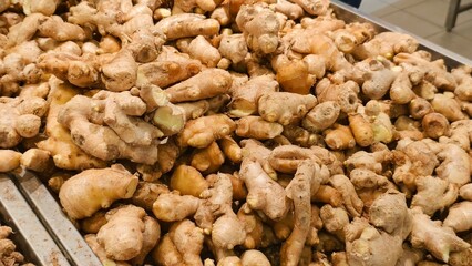 Fototapeta premium A high-angle shot shows a large heap of raw, knobby ginger roots arranged on a metal retail tray at a grocery store fresh produce section.