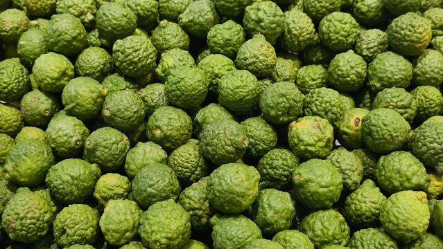 An overhead full-frame shot captures a dense collection of bumpy-skinned kaffir limes, showing their distinct wrinkled texture at a fresh produce stall.