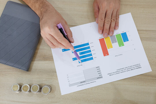 
Man sits at desk, thoughtful, pen in hand. Piggy bank and coins rest nearby, symbolizing savings. He sketches ideas on notebook, surrounded by charts. Office shelves hold colorful folders