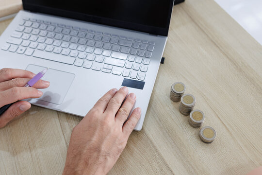 
Man sits at desk, thoughtful, pen in hand. Piggy bank and coins rest nearby, symbolizing savings. He sketches ideas on notebook, surrounded by charts. Office shelves hold colorful folders