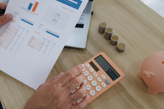 
Man sits at desk, thoughtful, pen in hand. Piggy bank and coins rest nearby, symbolizing savings. He sketches ideas on notebook, surrounded by charts. Office shelves hold colorful folders