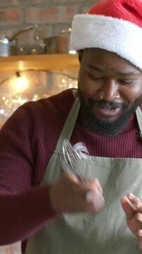 Vertical video: Laughing cook in Santa hat apron reaching whisk stirring at kitchen counter to bake