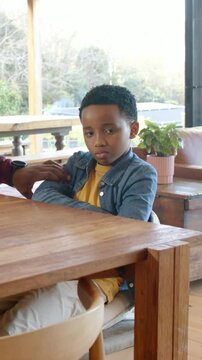 Vertical video: Reaching adult hand touching boy's arm at table in yellow tee, comforting